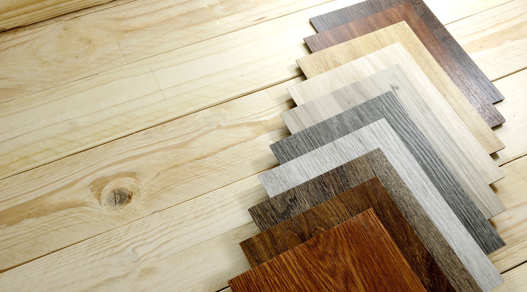 A fan of flooring samples in wood, grey and stone finishes laid out on a pale timber floor